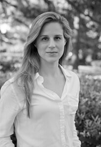 A black and white image of a white woman standing in front of trees and bushes